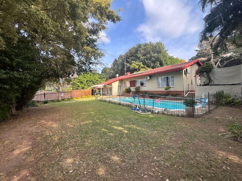 Spacious rear garden featuring a swimming pool with safety fencing, mature trees, and a view of the townhouse rear elevation.