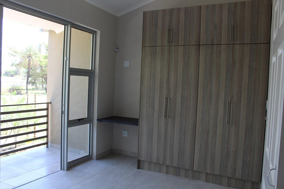 A bright bedroom featuring built-in wood-grain cabinetry, a small integrated desk, and sliding glass doors opening onto a private balcony.