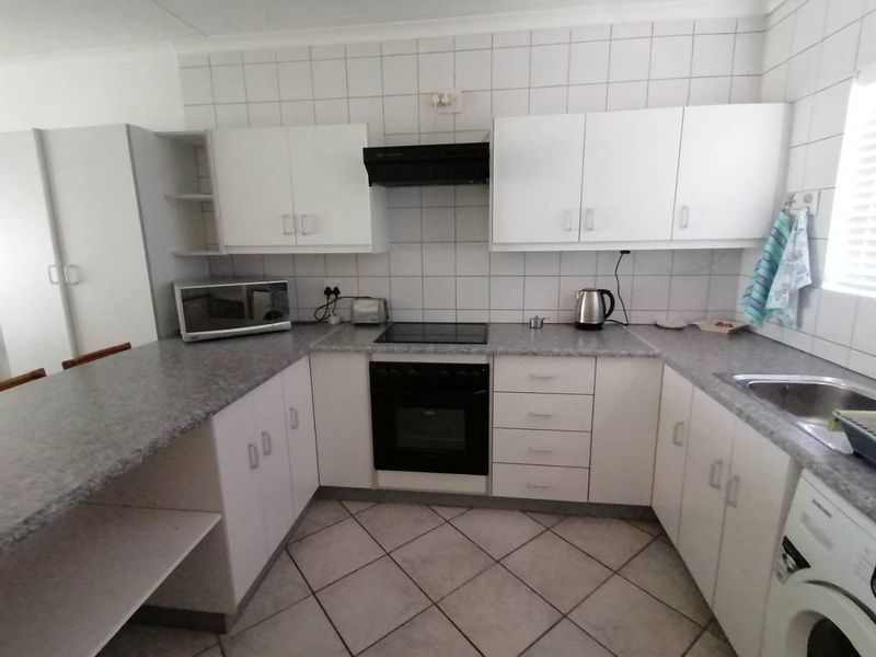 A functional kitchen featuring white cabinetry, a built-in oven with hob, extractor fan, and tiled flooring with a breakfast bar counter.