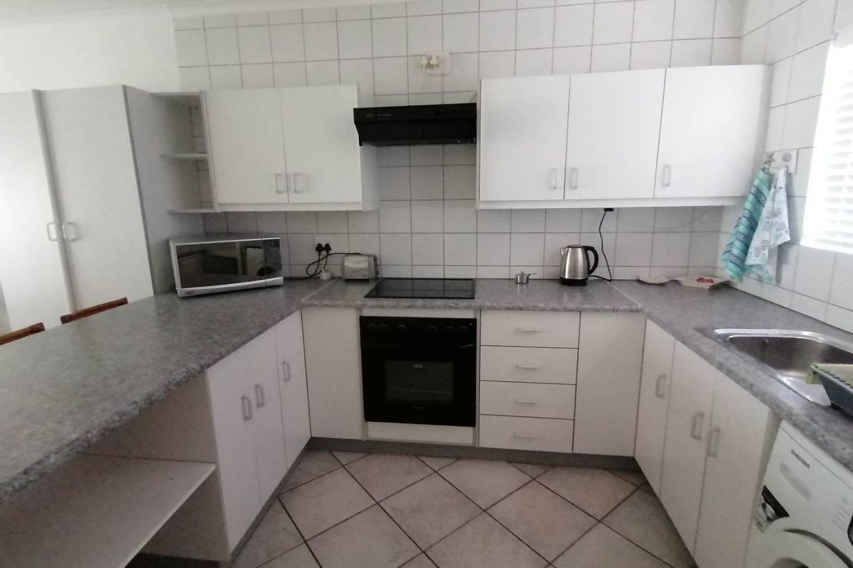 A functional kitchen featuring white cabinetry, a built-in oven with hob, extractor fan, and tiled flooring with a breakfast bar counter.