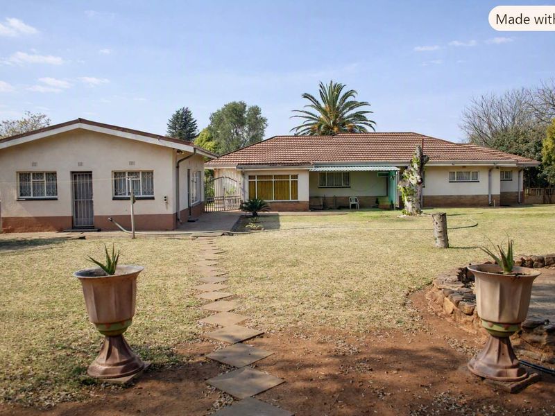 Rear view of the property featuring a spacious garden, paved walkway, and two separate building structures with tiled roofs.
