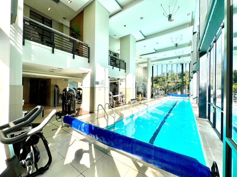 Modern indoor lap pool area featuring floor-to-ceiling windows, tiled flooring, and a mezzanine level overlooking the swimming facility.