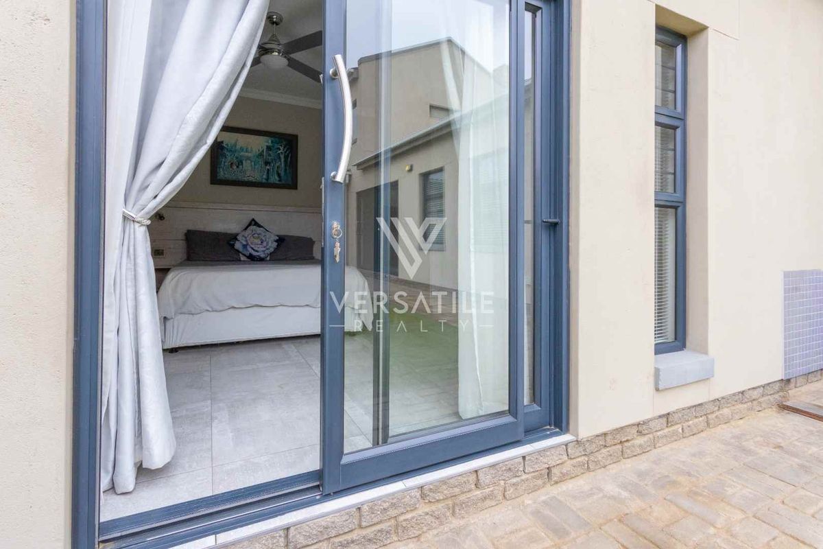 A view from a paved patio looking into a bedroom through a modern sliding glass door, featuring tiled floors and a ceiling fan.