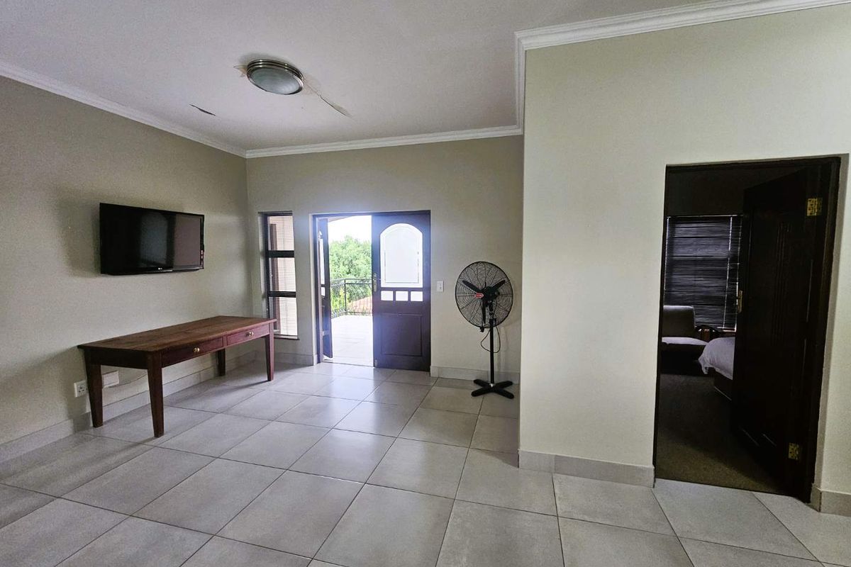 Spacious living area featuring large format floor tiles, crown molding, and direct access to an outdoor balcony through a wooden door.