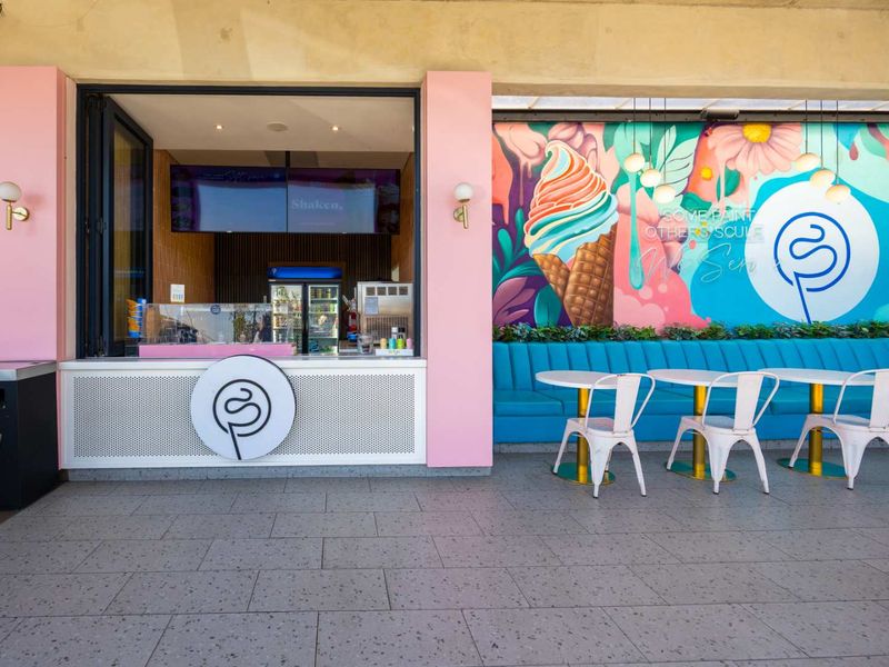 A vibrant outdoor patio area featuring a service counter, fixed blue banquette seating, and a decorative mural, ideal for a cafe or dessert shop.