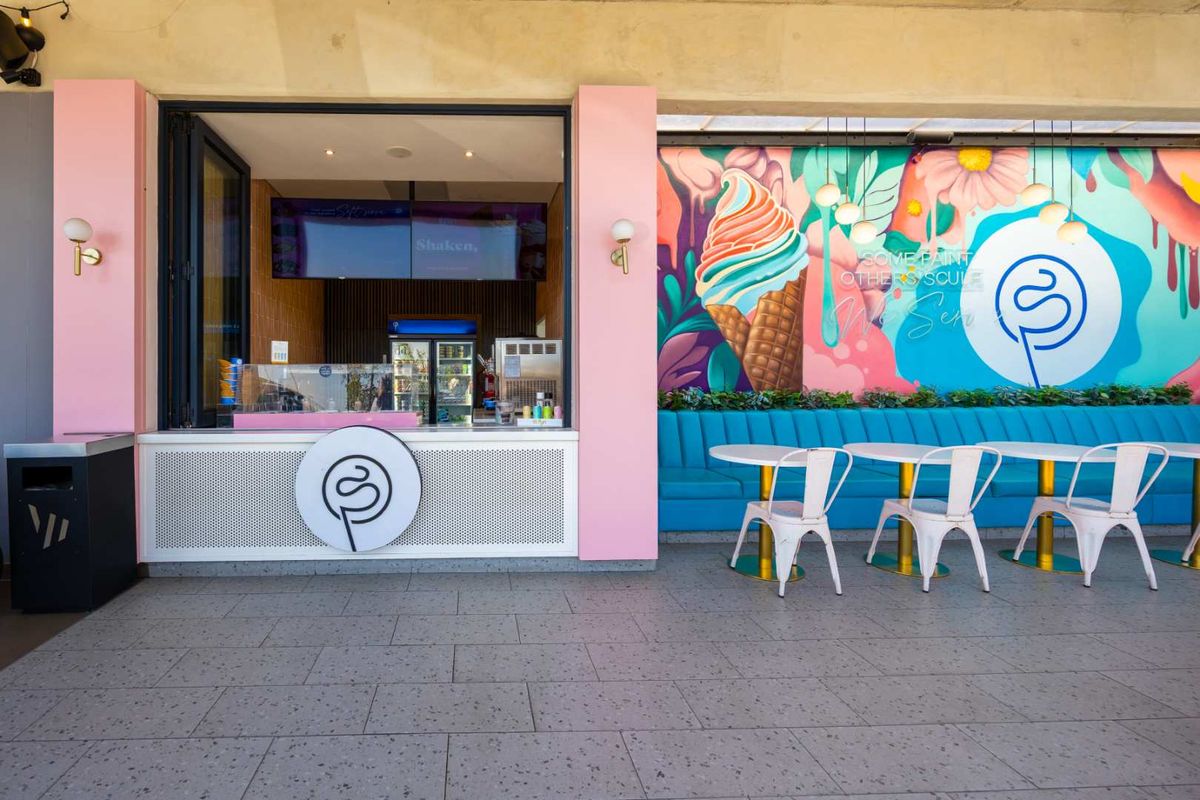 A vibrant outdoor patio area featuring a service counter, fixed blue banquette seating, and a decorative mural, ideal for a cafe or dessert shop.
