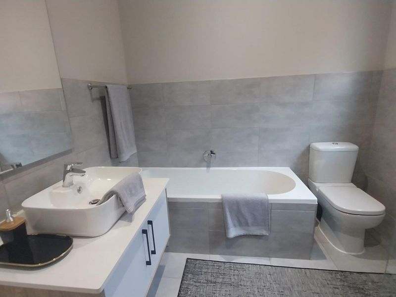 Modern bathroom featuring a built-in vanity with vessel sink, a bathtub, and a toilet, finished with neutral grey wall and floor tiles.