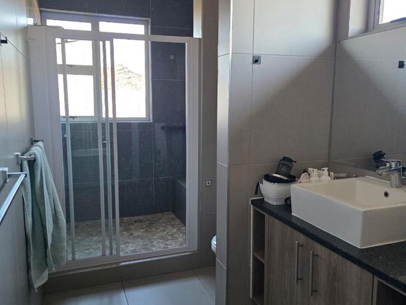Modern bathroom featuring a glass-enclosed shower, a vanity with a vessel sink, and neutral floor-to-ceiling tiling.