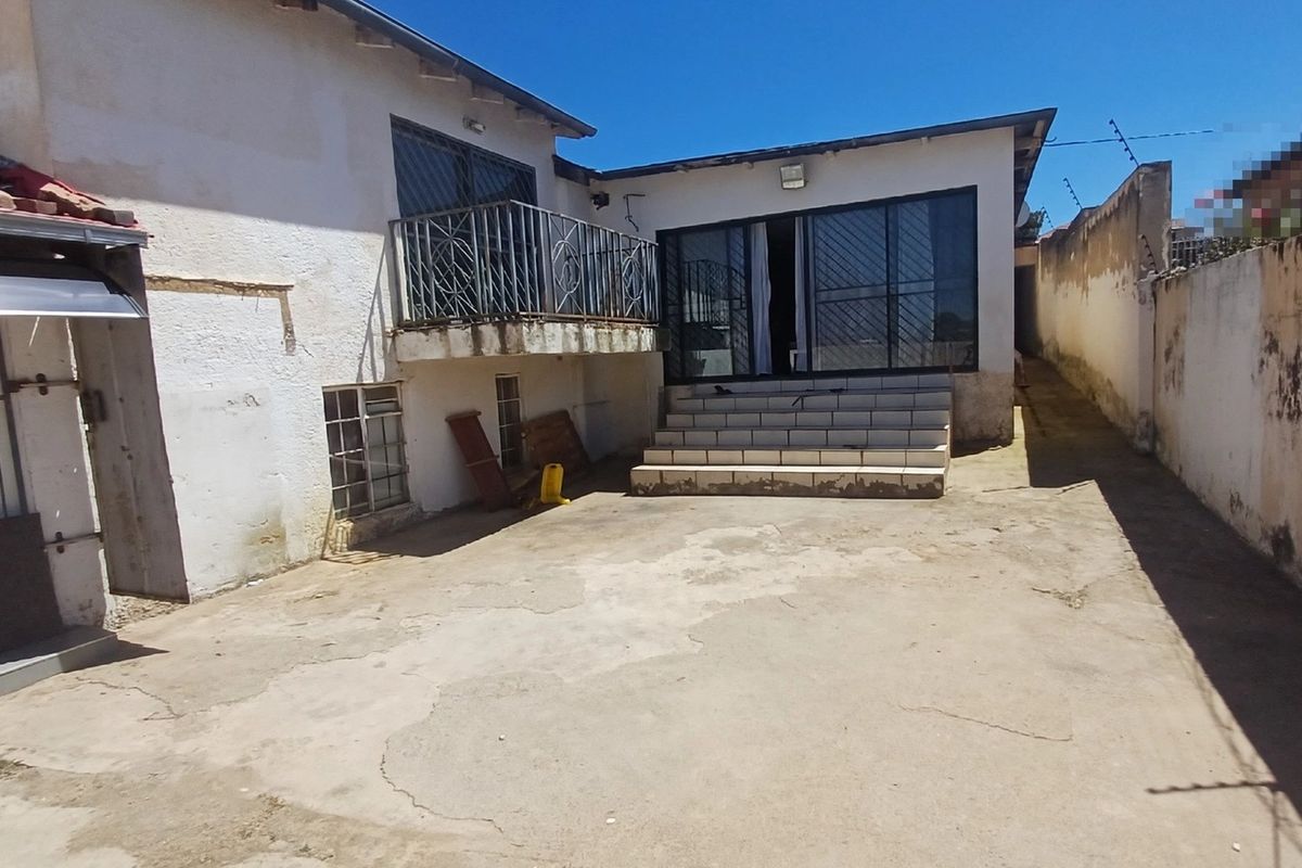 Rear exterior view of the property featuring a concrete patio, tiled steps leading to a sliding door, and a balcony with metal railings.