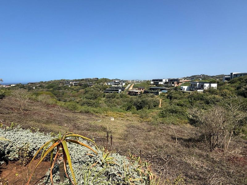 A wide-angle view of the vacant residential land featuring natural coastal vegetation and surrounding estate developments in the distance.