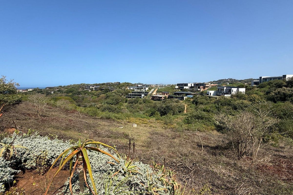 A wide-angle view of the vacant residential land featuring natural coastal vegetation and surrounding estate developments in the distance.
