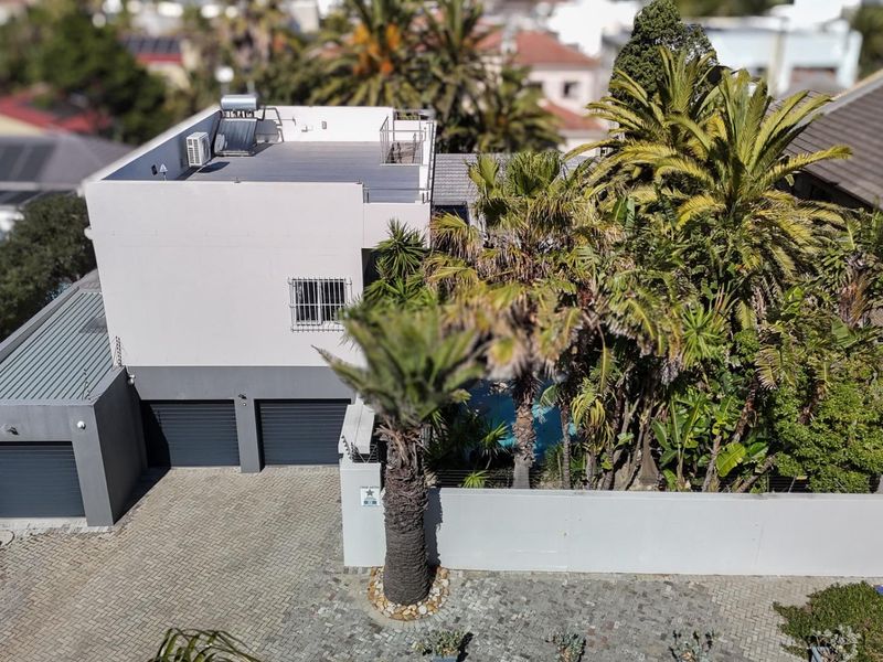 Aerial view of the property featuring a multi-car garage, paved driveway, and flat roof with solar water heating system.