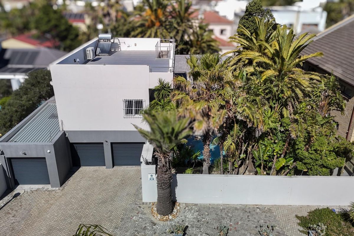 Aerial view of the property featuring a multi-car garage, paved driveway, and flat roof with solar water heating system.