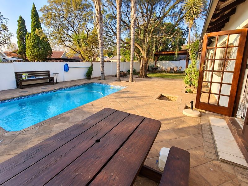 Outdoor pool area featuring a tiled patio, swimming pool, and a rear garden with a pergola, accessible via a wooden door.