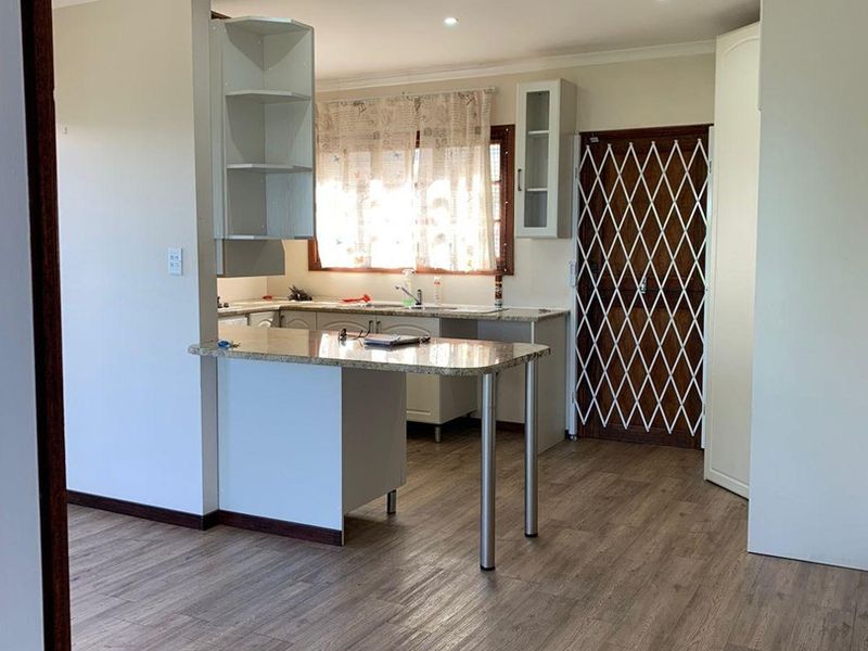 A bright, open-plan kitchen featuring granite countertops, ample built-in cabinetry, and modern laminate flooring, providing a clean and functional space.