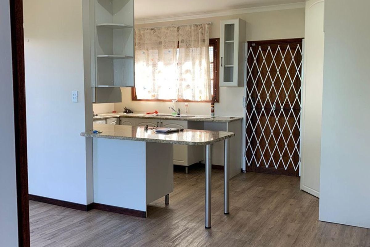 A bright, open-plan kitchen featuring granite countertops, ample built-in cabinetry, and modern laminate flooring, providing a clean and functional space.