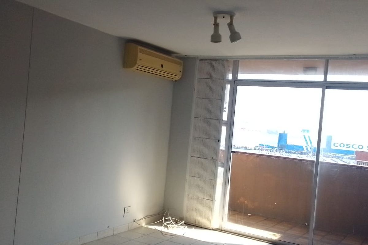 An empty living room featuring tiled floors, a wall-mounted air conditioning unit, and large sliding glass doors leading to a balcony with an urban view.