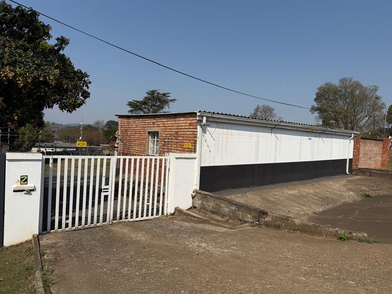 Front exterior view of the property featuring a metal security gate, brick and painted wall facade, and a concrete driveway entrance.