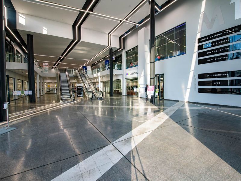 Spacious modern industrial atrium featuring polished tile flooring, structural steel columns, integrated linear lighting, and dual escalators leading to upper levels.