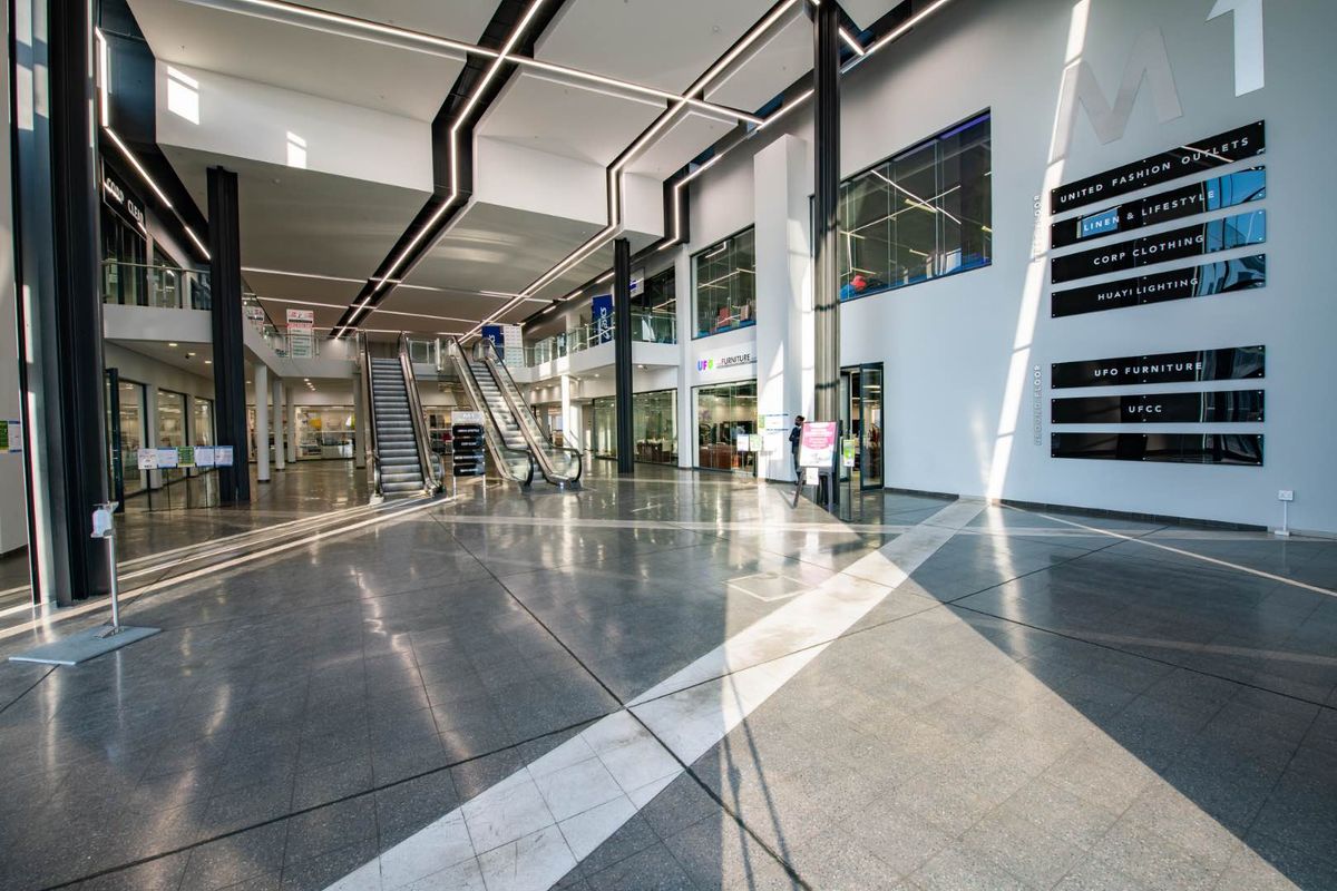 Spacious modern industrial atrium featuring polished tile flooring, structural steel columns, integrated linear lighting, and dual escalators leading to upper levels.