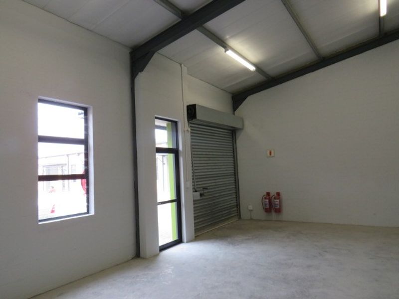 Spacious industrial utility area featuring concrete flooring, exposed steel structural beams, roller shutter door access, and functional fluorescent lighting.
