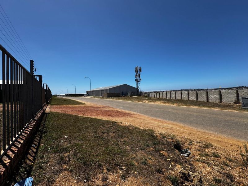 Street view of the industrial property featuring a paved access road, secure perimeter fencing, and a prominent telecommunications tower on site.