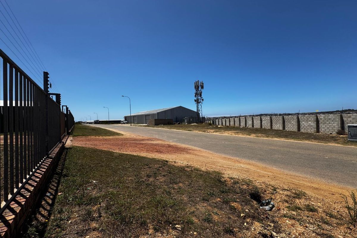 Street view of the industrial property featuring a paved access road, secure perimeter fencing, and a prominent telecommunications tower on site.