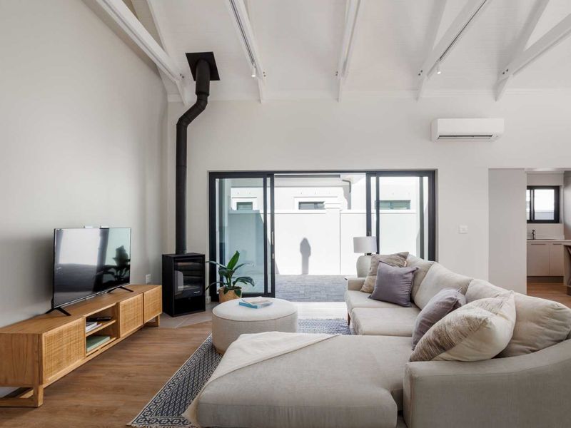 Bright open-plan living area featuring vaulted ceilings with exposed rafters, a modern freestanding fireplace, and seamless access to the outdoor patio through sliding doors.