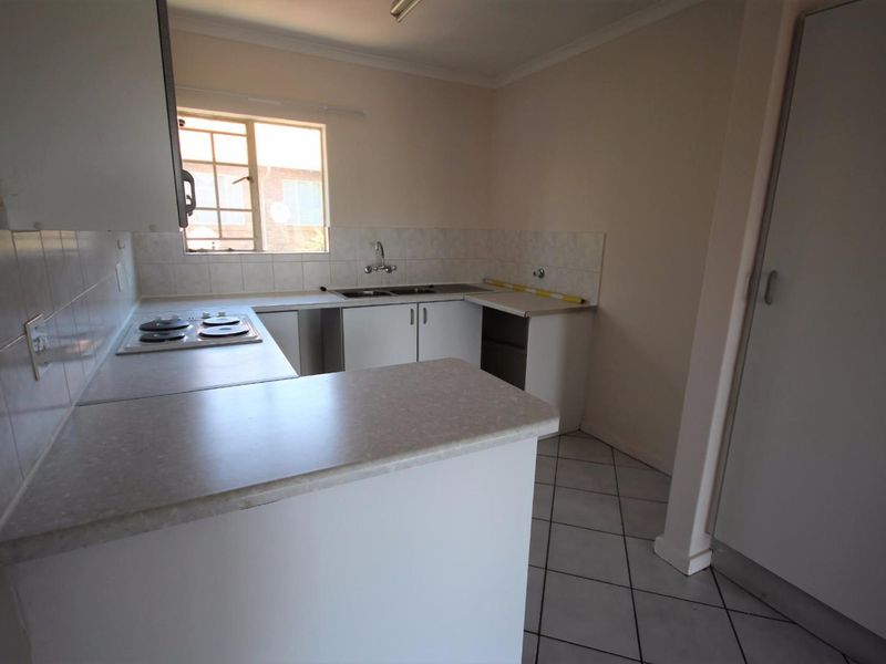 A functional kitchen featuring built-in cabinetry, laminate countertops, an electric hob, and a double sink, with tiled flooring and backsplash.