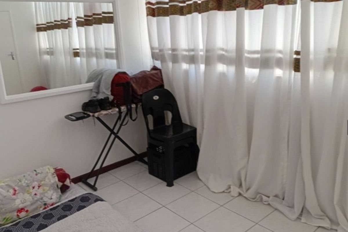 A bedroom featuring tiled flooring and a wall-mounted mirror, providing a functional space with neutral finishes.
