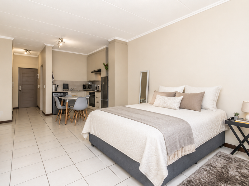 An open-plan studio apartment featuring a compact kitchen area with built-in cabinetry and tiled flooring throughout the living and sleeping space.