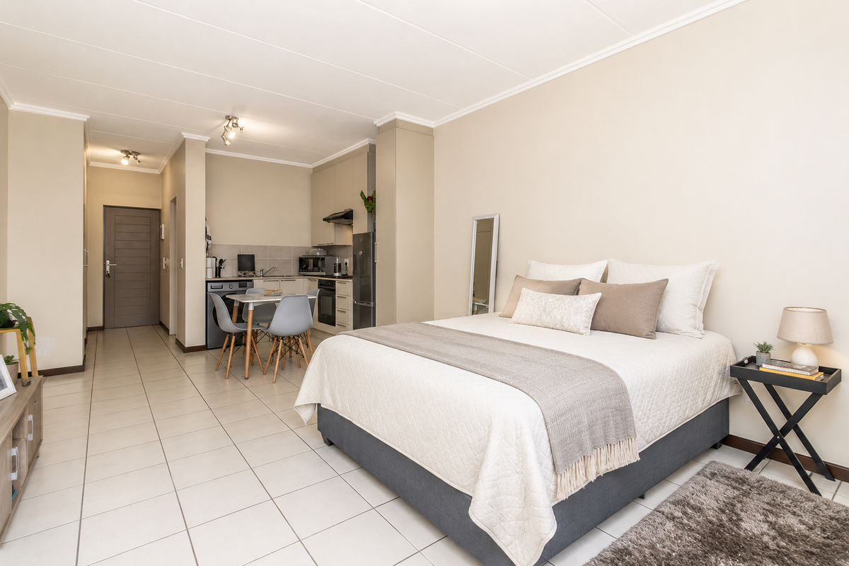 An open-plan studio apartment featuring a compact kitchen area with built-in cabinetry and tiled flooring throughout the living and sleeping space.