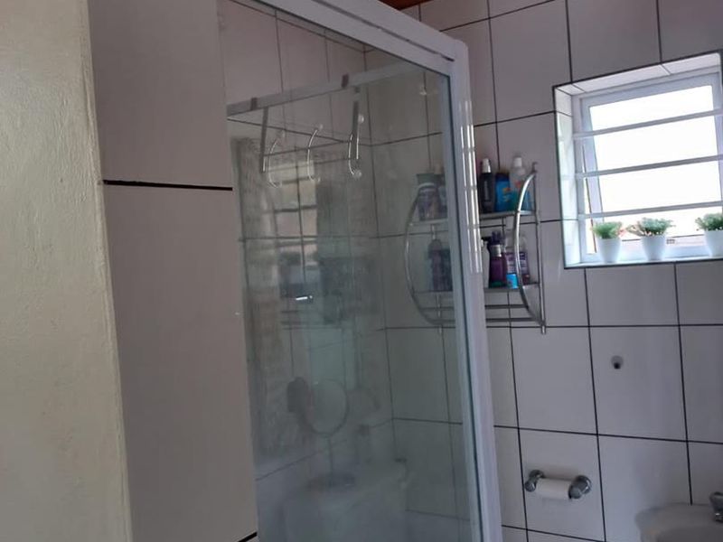 A functional bathroom featuring a shower enclosure, toilet, washbasin, and tiled walls with a timber ceiling.