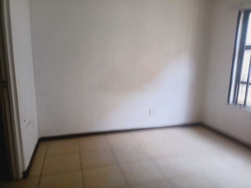 An empty bedroom featuring tiled flooring and a window with security bars, requiring minor cosmetic updates to the walls.