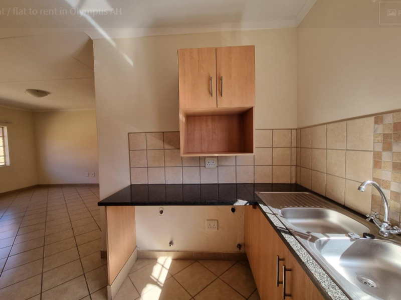 A functional kitchen area featuring granite countertops, double stainless steel sink, and tiled finishes, with an open-plan layout leading to the living space.