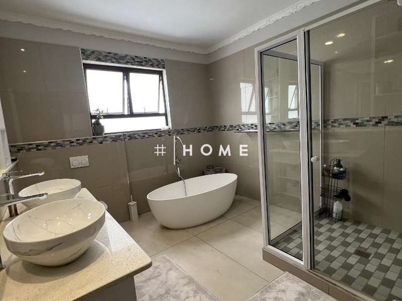Modern bathroom featuring a freestanding bathtub, glass-enclosed shower, and a double vanity with vessel sinks, finished with contemporary wall and floor tiles.