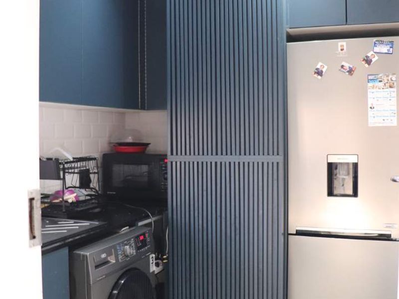 A modern scullery featuring dark blue cabinetry, a sliding slatted barn door, subway tile backsplash, and tiled flooring.