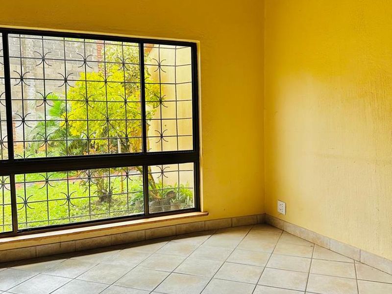 A bright, empty bedroom featuring tiled flooring, a large window with security bars, and yellow painted walls.