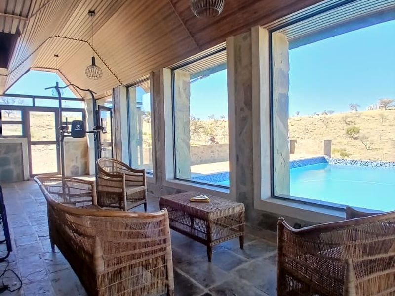 Spacious covered patio featuring a vaulted timber ceiling, stone flooring, and large windows overlooking the swimming pool and surrounding landscape.