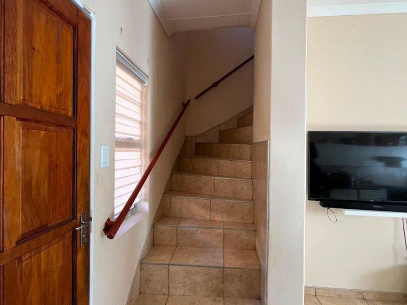 A tiled staircase with a wooden handrail leading to the upper level, featuring ceramic floor tiles and neutral wall finishes.