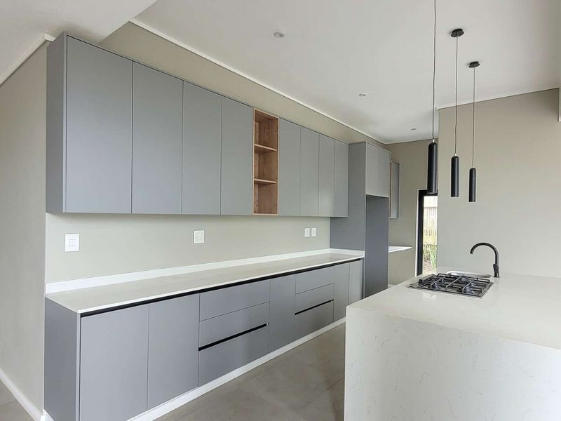 Modern kitchen featuring sleek grey cabinetry, stone countertops, a central island with a gas hob, and contemporary pendant lighting.