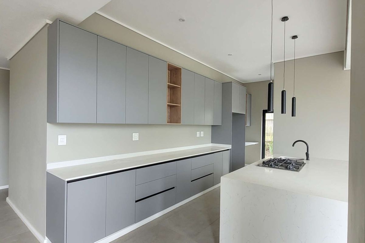 Modern kitchen featuring sleek grey cabinetry, stone countertops, a central island with a gas hob, and contemporary pendant lighting.