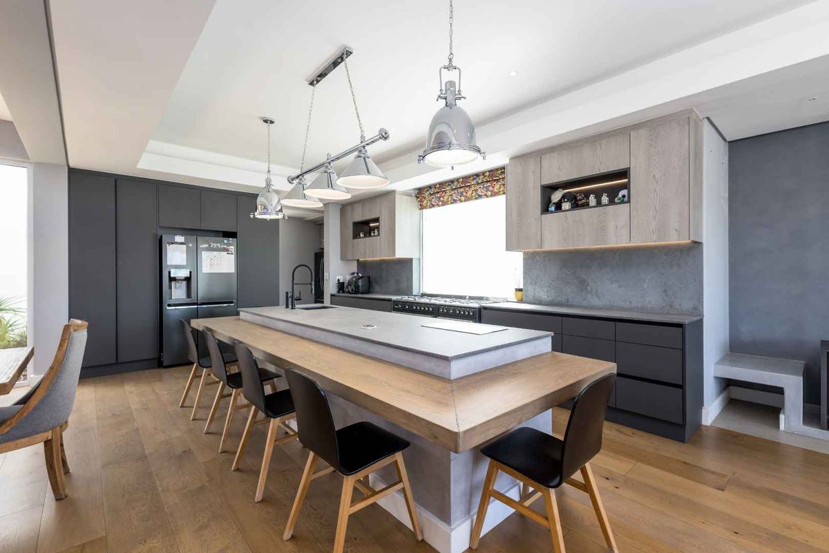 Modern kitchen featuring a large central island with stone countertop, dark cabinetry, integrated appliances, and high-quality hardwood flooring.