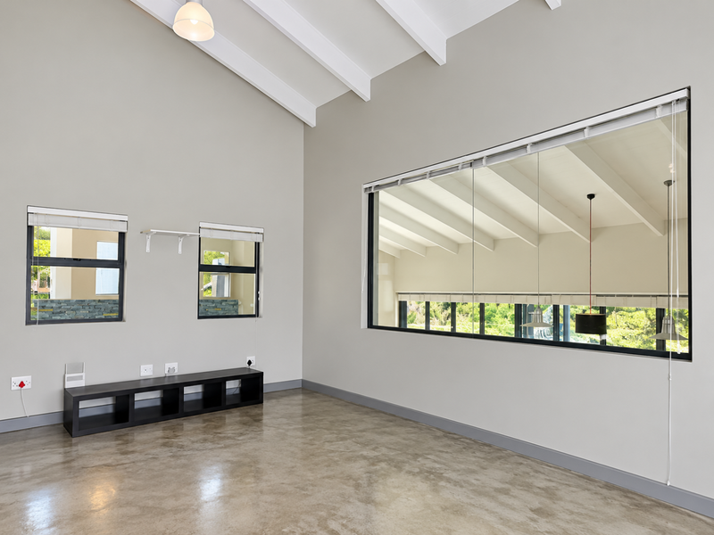 Spacious living area featuring high vaulted ceilings with exposed rafters, polished concrete floors, and a large picture window providing ample natural light.