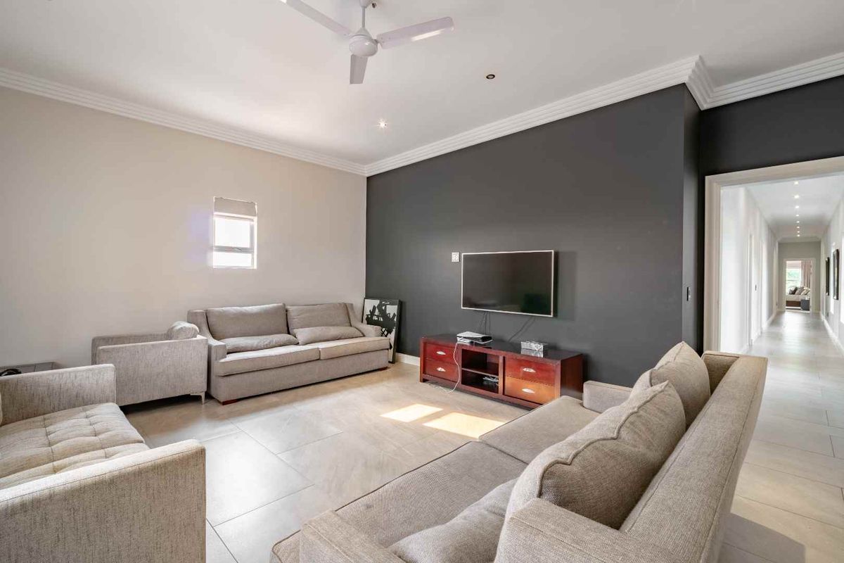 Spacious living room featuring tiled flooring, a feature wall, and a ceiling fan, leading into a long hallway.