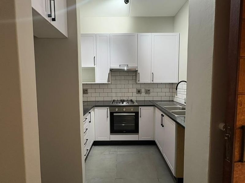 A modern, U-shaped kitchen featuring white cabinetry, subway tile backsplash, dark countertops, and integrated stainless steel appliances.