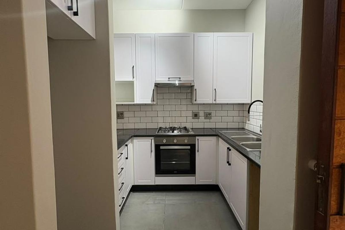 A modern, U-shaped kitchen featuring white cabinetry, subway tile backsplash, dark countertops, and integrated stainless steel appliances.