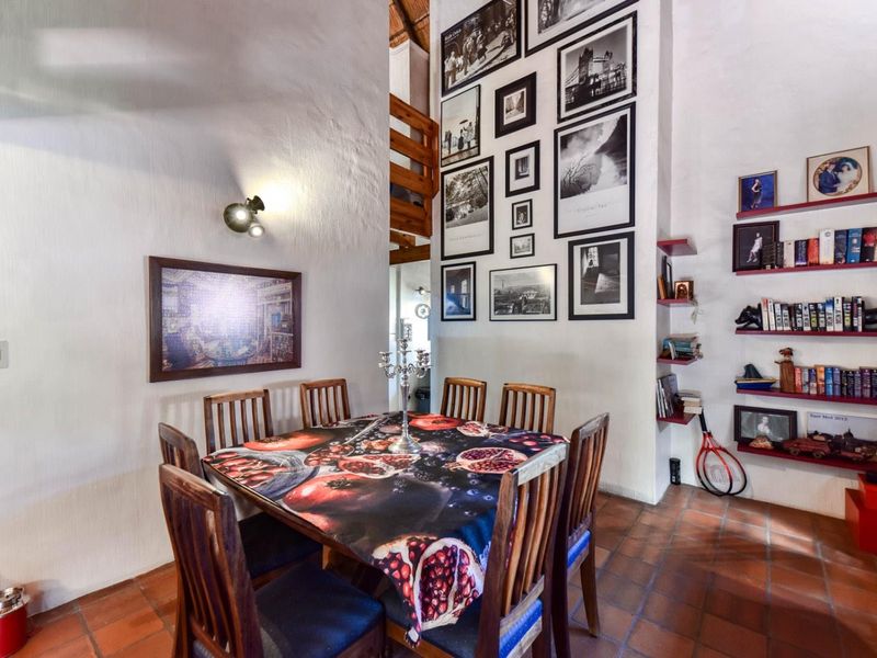 Dining area featuring terracotta floor tiles, built-in wall shelving, and a double-height ceiling with a visible mezzanine level.