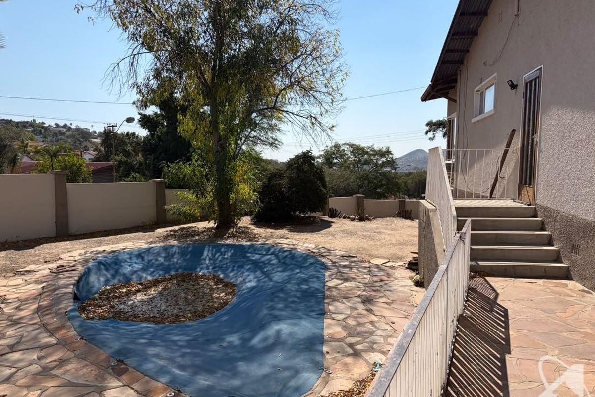Rear garden area featuring a swimming pool with a cover, stone paved patio, and concrete stairs leading to the house exterior.