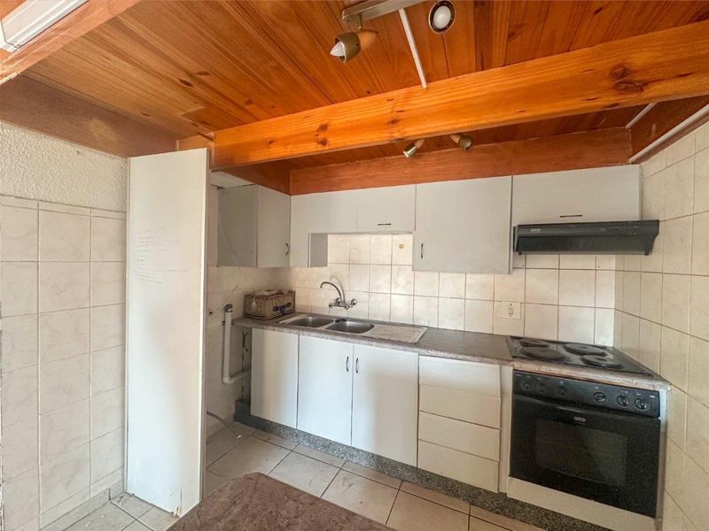 Compact kitchen featuring built-in cabinetry, electric stove with extractor fan, tiled backsplash, and exposed timber ceiling beams.